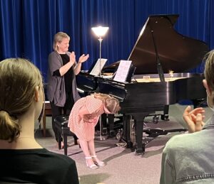 A person wearing pink bowing in front of the piano