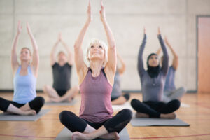 A group of adults are doing yoga in a fitness center. They are raising their arms into the air.