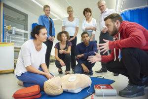 The first picture is a a mixed age group listen to their tutor as he shows the procedure involved to resuscitate using a defibrillator .  The second picture is of two people practicing CPR